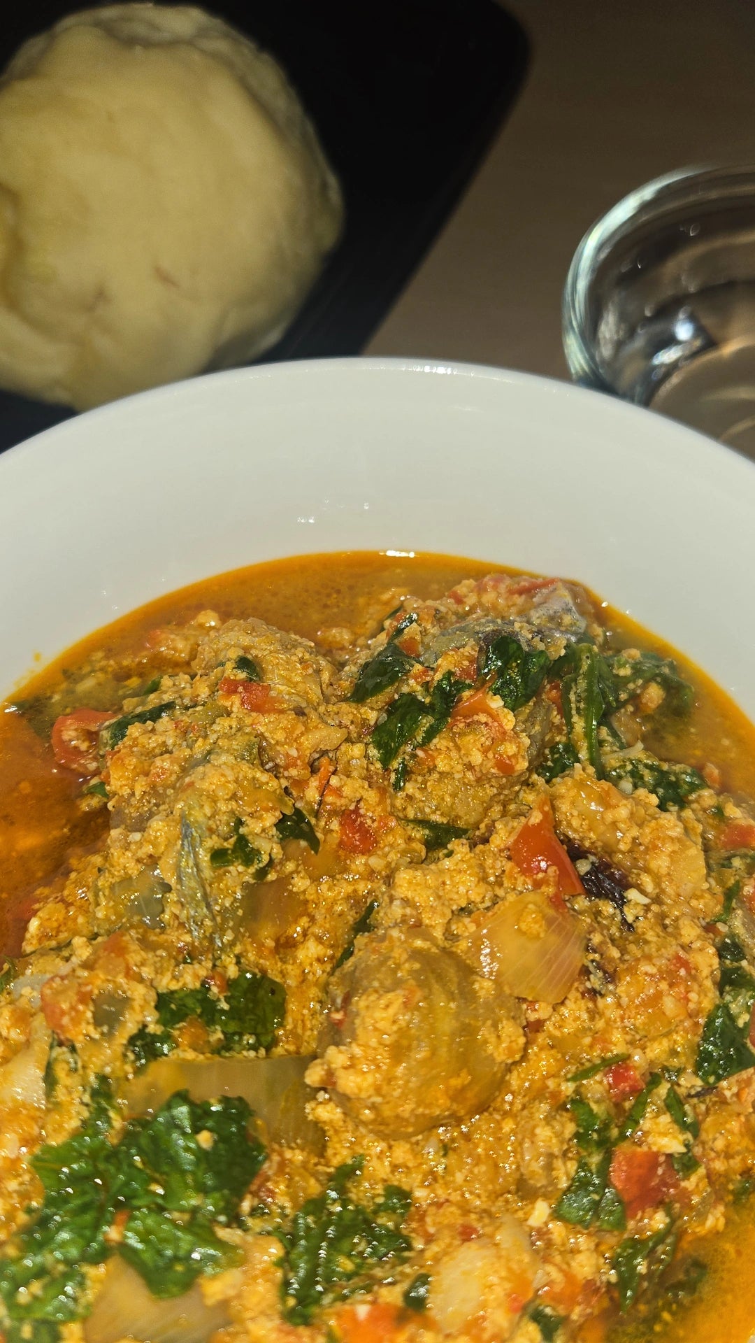 Egusi soup with leafy greens and tomatoes served in a white bowl