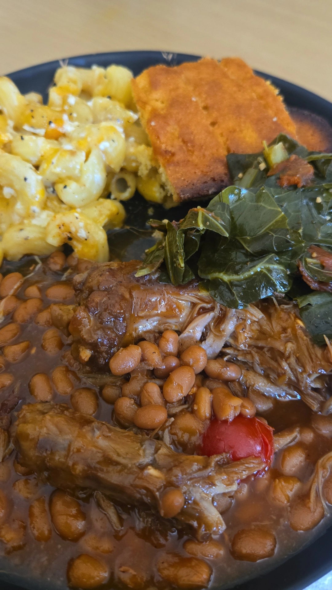 Soul food plate with macaroni and cheese, cornbread, collard greens, beans and braised meat