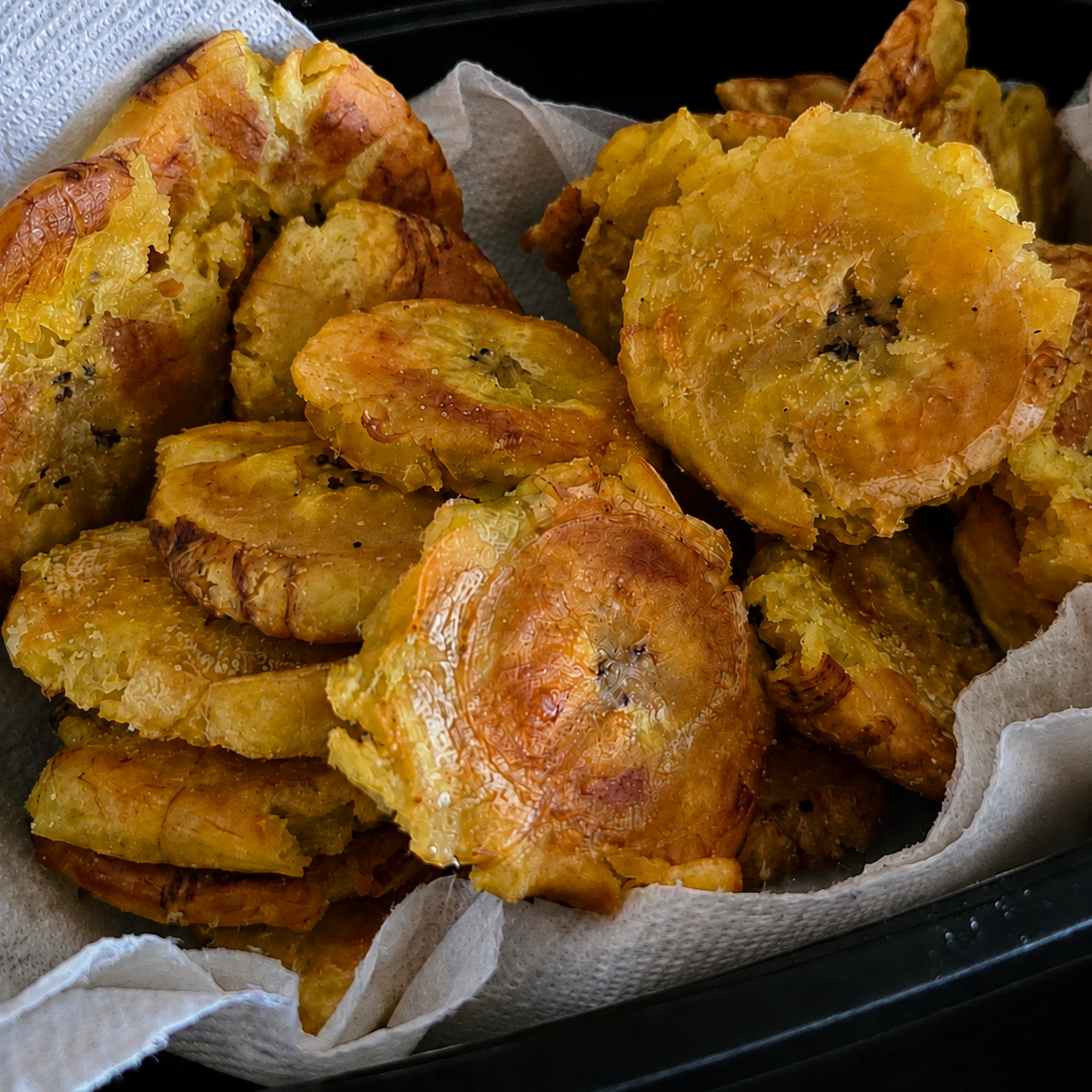 Golden twice-fried patacones piled in a serving tray